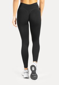 Leggings nere a vita alta e vestibilità aderente, realizzate in materiale elasticizzato. Il modello indossa sneakers bianche con suole scure.
