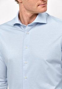 Lichtblauwe overhemden met een spread collar, subtiele textuur en witte knopen aan de voorkant, met een slank ontwerp.