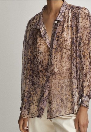 Transparente, langärmelige Bluse mit braunem und lila Leopardenmuster, ungeplant über weißen Hosen getragen.