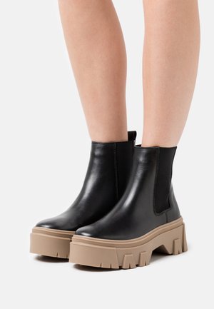 Bottines en cuir noir avec une semelle plateforme épaisse beige, dotées de panneaux latéraux en élastique et d'une texture lisse.