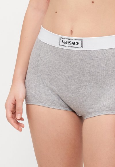 Szürke pamut boxer alsónadrág, fehér elasztikus derékkal, amelyen a "VERSACE" logó található. Közelkép a derékról és a nadrág oldaláról.