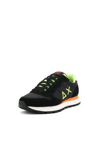 Sneaker nera con lacci e accenti verde neon. Presenta materiali in suede e mesh, logo triangolare e una suola arancione a contrasto.