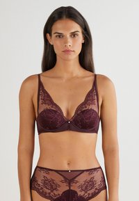 Soutien-gorge en dentelle bordeaux avec armatures, motif floral transparent, bretelles réglables et un petit accent à l'avant. Culotte assortie en dentelle transparente.