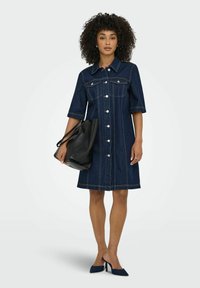 Jeansklänning med krage, korta ärmar, knapprad fram och vit sömnad. Tillsammans med en svart axelväska och marinblå klackar.