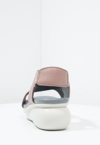 Sandal aperto rosa e grigio con suola chunky bianca esposta su una superficie bianca contro uno sfondo bianco.