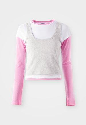 Top cinza sem mangas sobre uma camisa de manga longa branca, com mangas rosa claro que se estendem além do cinza, apresentando uma textura canelada.
