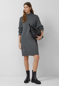 Graues Strickkleid mit hohem Kragen, gerippten Bündchen und strukturierten Akzenten, kombiniert mit einer schwarzen strukturierten Tasche und klobigen schwarzen Stiefeln.