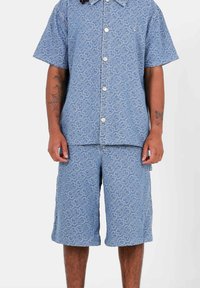 Camisa de botones de manga corta y pantalones cortos a juego, ambos en azul claro con un patrón de corazones repetido, hechos de tela texturizada.
