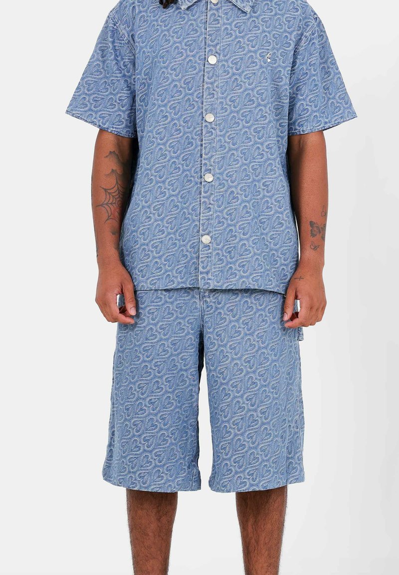 Camicia a maniche corte con bottoni e pantaloni corti abbinati, entrambi in blu chiaro con un motivo a cuori ripetuto, realizzati in tessuto testurizzato.