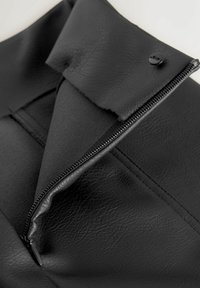 Pochette en simili cuir noir avec une surface texturée, dotée d'une fermeture éclair et d'une fermeture à pression, pliée en haut pour un accès facile.