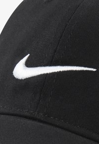 Musta lippalakki, joka on valmistettu vakosametista ja jossa on valkoinen kirjailtu Nike-logo edessä. Mallissa on pyöreä kruunu ja kaareva lippa.