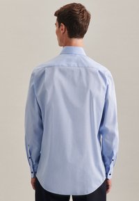 Camicia a maniche lunghe azzurro chiaro con orlo curvo e dettagli in nero sui polsini. Tessuto morbido con un design semplice.