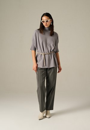 Haut en tricot gris avec un design côtelé, ceinturé à la taille, associé à un pantalon gris à rayures et des bottines blanches pointues.