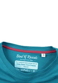 Teal T-shirt med en maroon rund halsudskæring, med hvid tekst og plejeetiket indeni. Lavet af 100% økologisk bomuld. Størrelseetiket synlig.