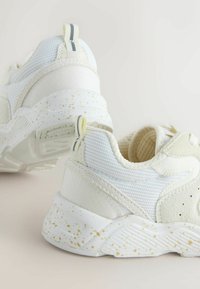 White athletic shoes with textured mesh and smooth panels. Features a speckled sole and rear pull tab with a gray stripe accent.