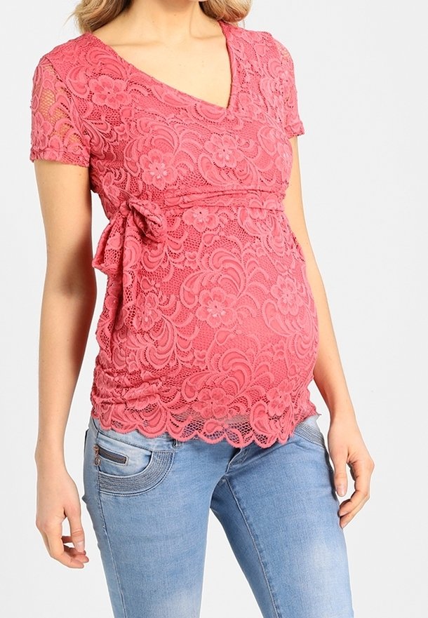 Haut de maternité en dentelle rose avec des manches courtes, un décolleté en v et un lien à la taille, agrémenté de motifs floraux et d'un design texturé.