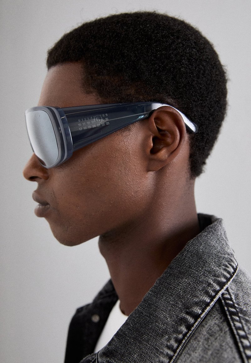 Sunglasses with dark blue frames and large, reflective lenses. Features a rectangular design with unique textural details along the arms.