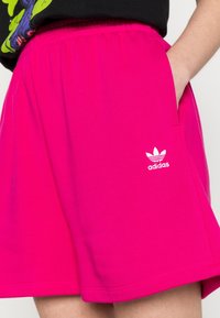 Pink cotton shorts with an elastic waistband, side pockets, and white Adidas logo detail. Smooth texture with a casual fit.