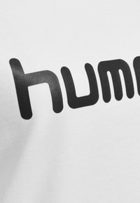 T-shirt bianca in cotone caratterizzata da un audace testo nero che scrive "hum". Il tessuto ha una texture liscia con un design pulito e minimal.