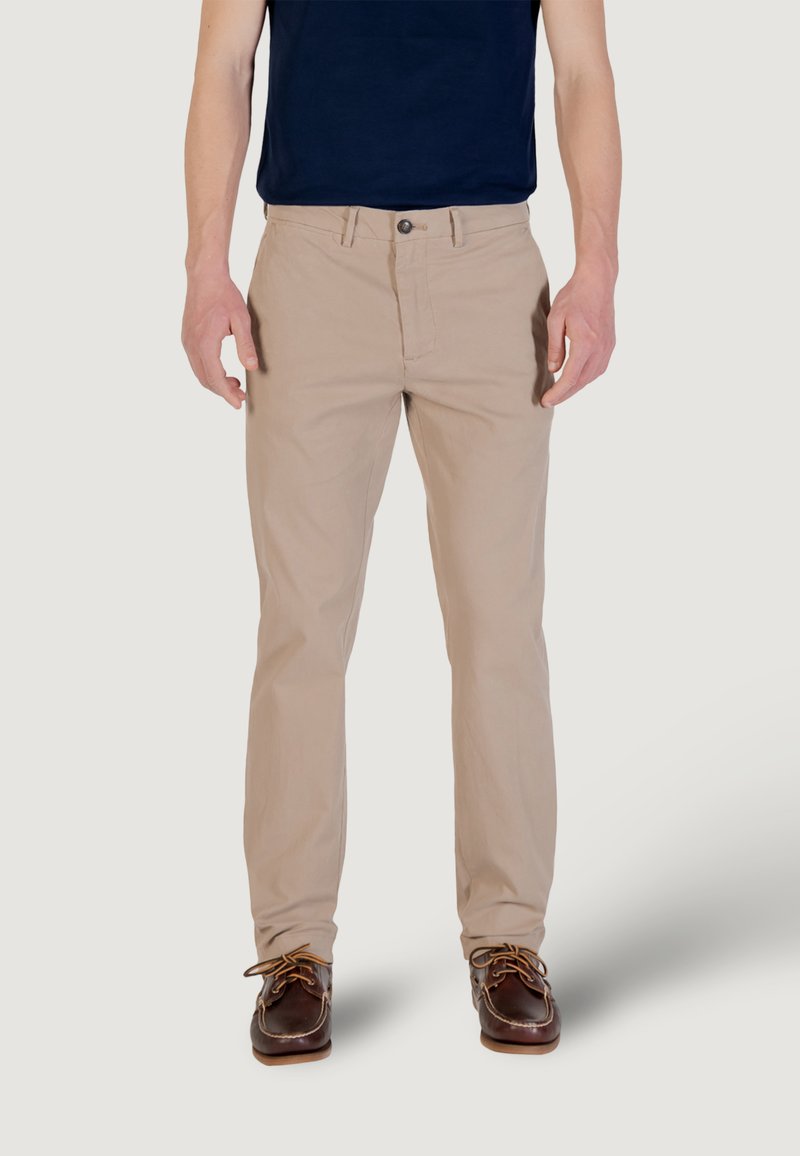 Chinos beige con vestibilità dritta, tasche frontali e chiusura con bottone. Indossati con una camicia blu navy e scarpe stringate marroni.