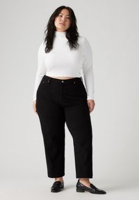 White long-sleeve turtleneck top with ribbed texture paired with high-waisted black jeans. Black loafers complete the outfit.