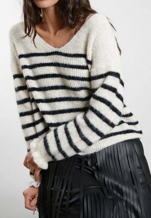 Maglione a righe colore crema con righe orizzontali nere, con scollo a V e vestibilità leggermente comoda. Indossato con una gonna plissettata in ecopelle nera.