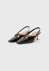 Zwarte gepatineerde leren slingback schoenen met spitse neuzen, kleine hakken en een subtiele gouden logo-detail dicht bij de enkelband.