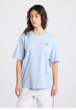 T-shirt en coton bleu clair à manches courtes et col rond. Présente un petit motif graphique rouge sur la poitrine. Coupe décontractée.