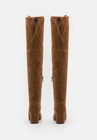 Botas marrones de ante sobre la rodilla con tacón bloque, cordones ajustables en la parte superior y cremalleras en los lados exteriores. Textura suave.