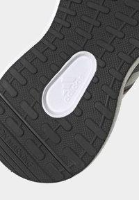 Suela de zapatilla de goma negra con un patrón texturizado, que presenta un logo blanco de Adidas y acentos en gris contrastante a lo largo del borde.