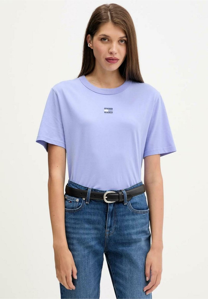 Světlofialové bavlněné tričko s krátkými rukávy, kulatým výstřihem a malým logem na hrudi. Doplněno modrými džínami a černým páskem.