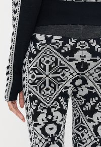 Zwart en grijs gemusterde leggings met ingewikkelde ontwerpen met geometrische en bloemmotieven, gemaakt van een zachte, gebreide stof.