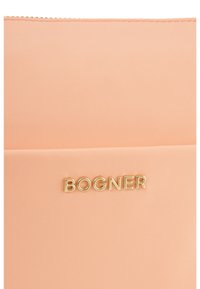 Nylonová taška v broskyňovej farbe s uzatváraním na zips a zlatým logom "BOGNER" na prednej strane, s hladkou textúrou a minimalistickým dizajnom.