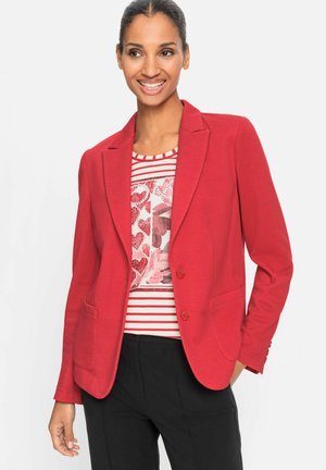 Blazer ajusté rouge avec un col cranté, deux boutons et des poches latérales, porté sur un haut à motifs avec des rayures. Texture de tissu lisse.