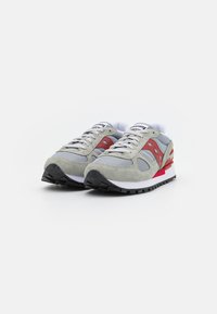 Sneaker in suede grigio e rete con dettagli rossi, logo bianco e suola ammortizzata. Presenta una suola testurizzata per la presa e chiusura con lacci.