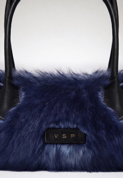 Sac à main bleu marine duveteux avec des poignées en cuir noir et une étiquette noire avec des lettres dorées VSP au centre avant.