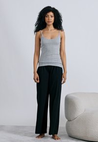 Débardeur gris à côtes et pantalon noir à jambes larges, tous deux en tissus doux. Le mannequin est pieds nus à côté d'un canapé crème texturé.