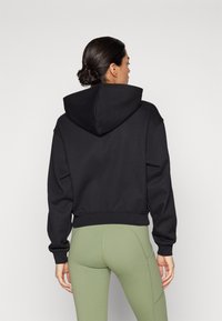 Black cropped hoodie featuring a drawstring hood and ribbed cuffs, paired with olive green stretch leggings. Smooth texture, relaxed fit.