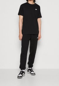 Svart Nike-t-shirt med en liten logotyp på bröstet, matchad med svarta sweatpants. Träningsskor med svart och vita designelement.