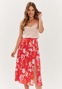 Květinová midi sukně v jasně červené barvě, s růžovými a bílými květinovými vzory, vysokým rozparkem, vyrobená z lehkého materiálu, doplněná o jemnou top camisole v barvě broskve.