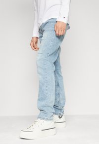 Ljusblå denimjeans med avslappnad passform, med synlig sömnad, rak benform och tillsammans med vita hög-top sneakers.
