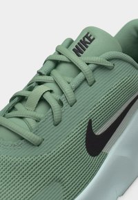 Πράσινο αθλητικό παπούτσι Nike με υφασμάτινη υφή, μαύρο λογότυπο swoosh και κορδόνια που περνούν μέσα από τρύπες σε λευκό φόντο.