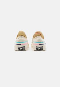 Beżowe trampki z płótna o fakturowej powierzchni, z wielokolorowymi akcentami na podeszwie oraz czarnym logo Converse All Star na pięcie.