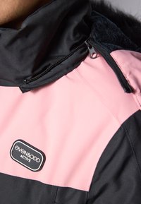 Rosa og svart jakke med høy krage, med en glidelåslomme, børstet stofffôr og en preget logo-lapp.