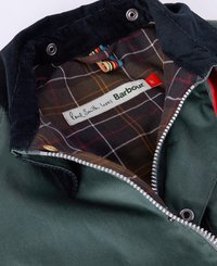 Casaco exterior verde com gola de veludo, fecho de zip e forro de xadrez multicolorido. O rótulo diz "Paul Smith ama Barbour."