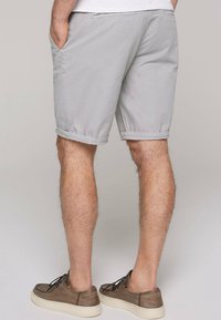 Grijze katoenen shorts met zijzakken, omgeslagen zoom en een relaxte pasvorm. Draagt met bruine casual schoenen.