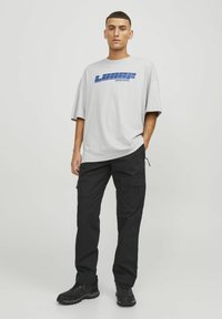 Pilkas per didelis t-shirt su mėlyna grafine užrašu, derinamas su juodais cargo kelnėmis su šoninėmis kišenėmis ir juodais tvirtais batais.