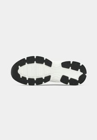 Μαύρη και λευκή σόλα αθλητικού παπουτσιού με έντονες ελαστικές αυλακώσεις, εξαγωνικά μοτίβα και υφασμένες περιοχές για κράτημα και υποστήριξη.