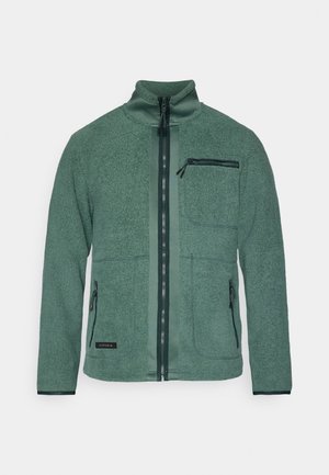 Veste en polaire verte avec un col haut, deux poches avant et une poche zippée sur la poitrine. Présente une fermeture éclair frontale lisse et un tissu texturé.