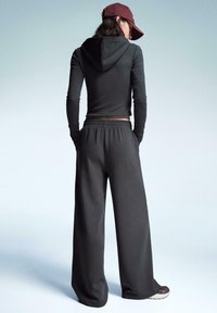 Sötétszürke kapucnis pulóver hosszú ujjal, amelyet laza szabású szürke nadrággal párosítanak. A hátsó nézet bemutatja a rugalmas derekú részletet és a laza lábbelit.